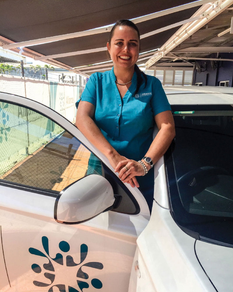 Driving Assessment and Remediation Smiling female driving trainer standing behind open car door