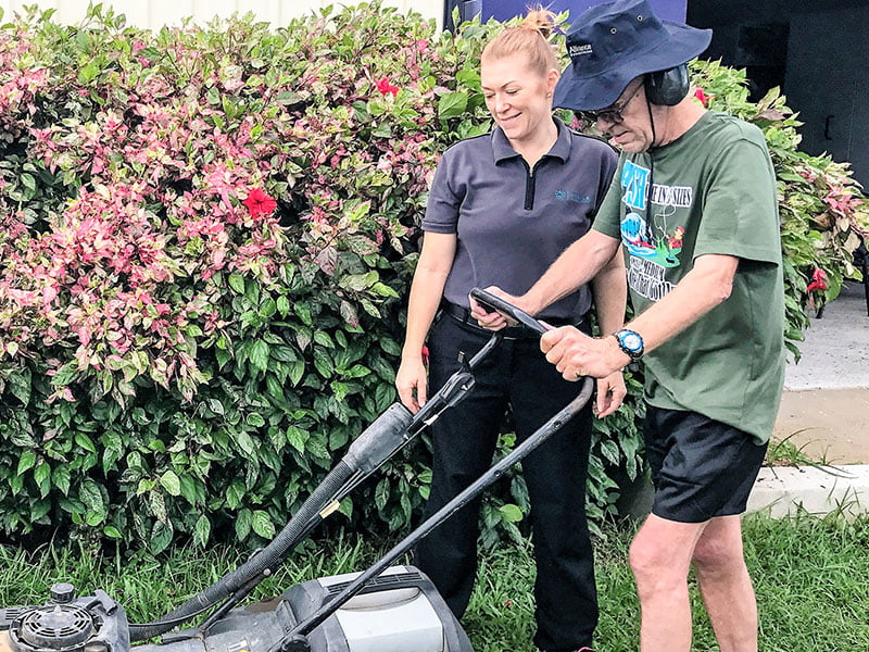 Exercise Physiology Townsville Rehab worker assisting elderly man to use a lawnmower